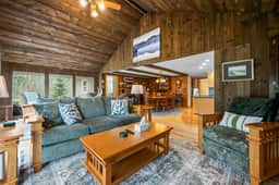 Cozy wood-clad great room with forest views, open dining, and comfy seating.